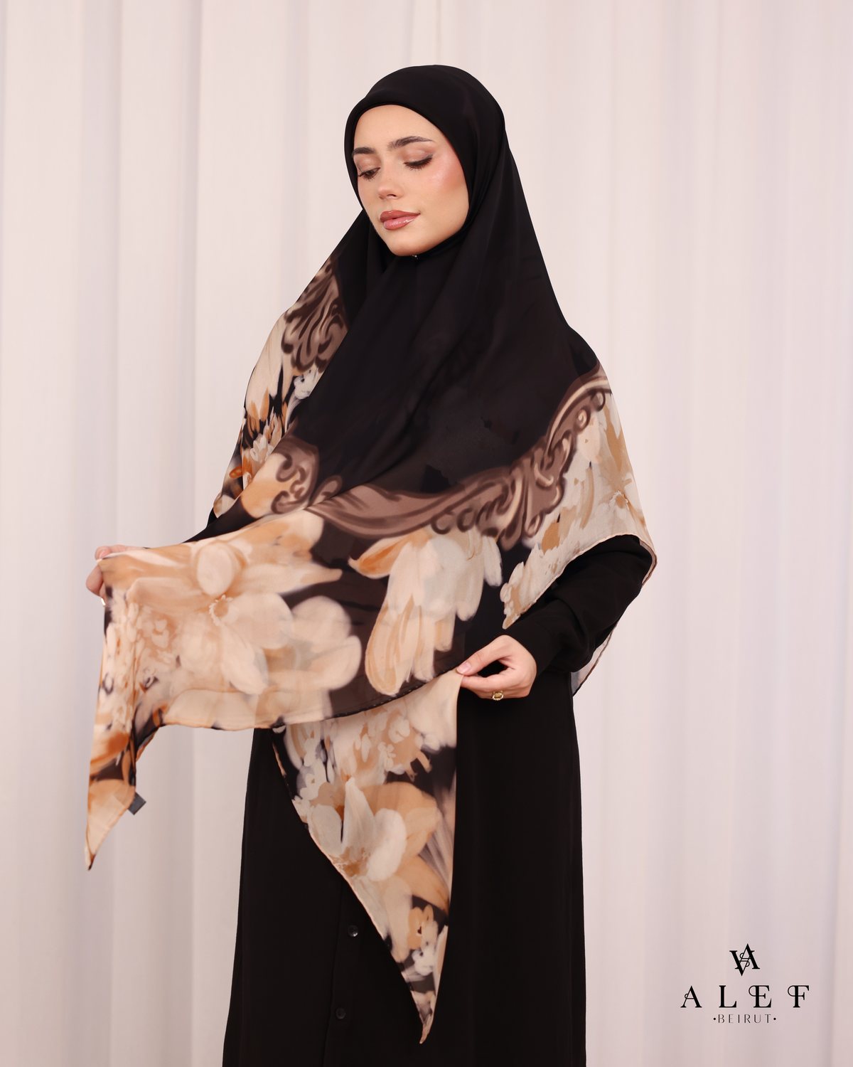 The Noir Baroque silk scarf, held open over a black abaya